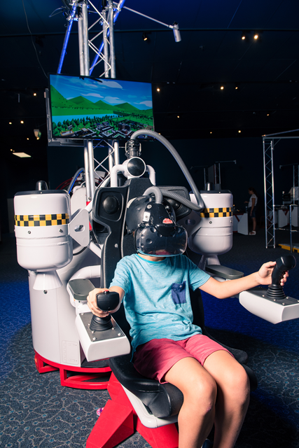 A young boy wearing a vr headset sitting in a jet pack simulator.