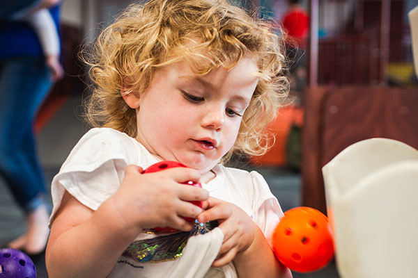 Toddler carrying plastic balls around in indoor play centre