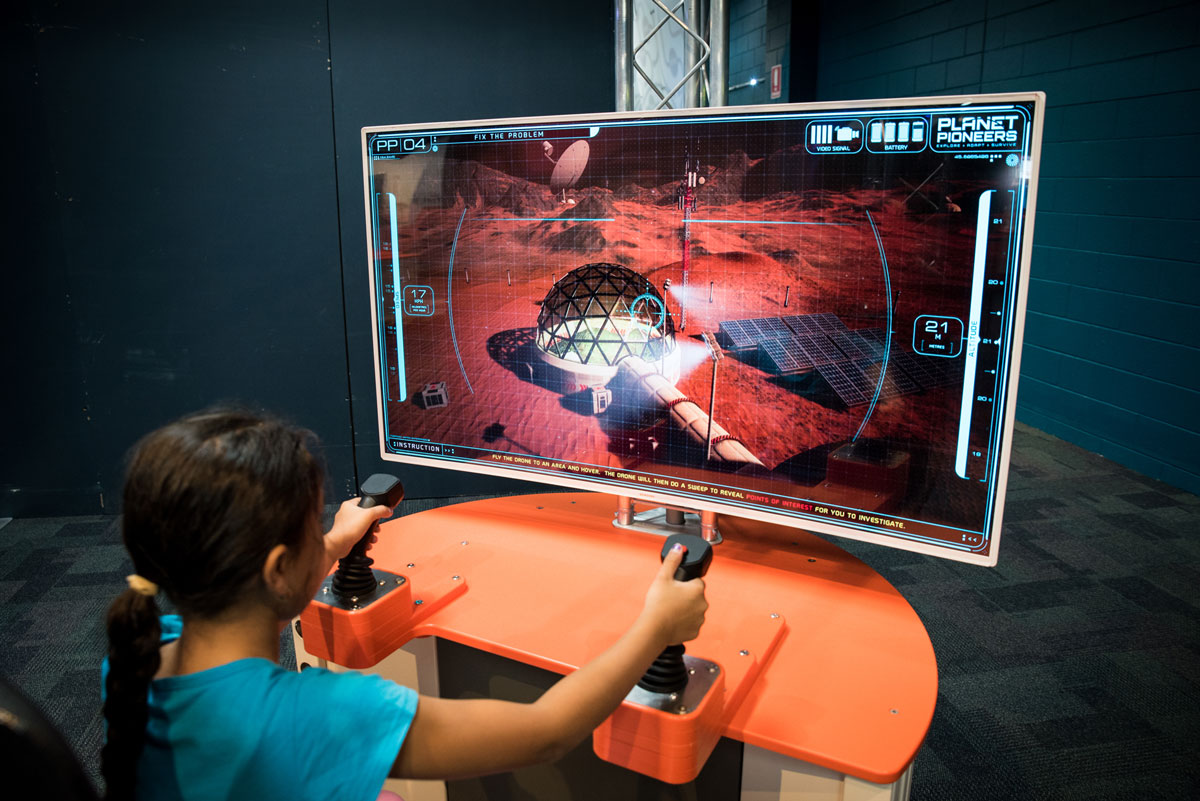 A young girl driving a mars rover near the space station in a simulator.