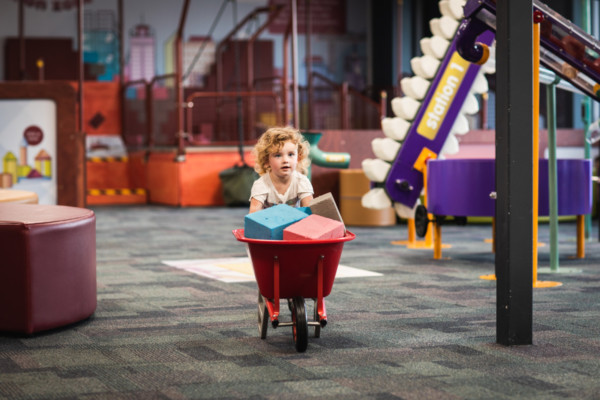 Young child pushing a wheelbarrow full of blocks in Discoverland.