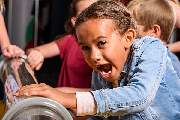 Young girl with her mouth open in excitement as she plays with an exhibit