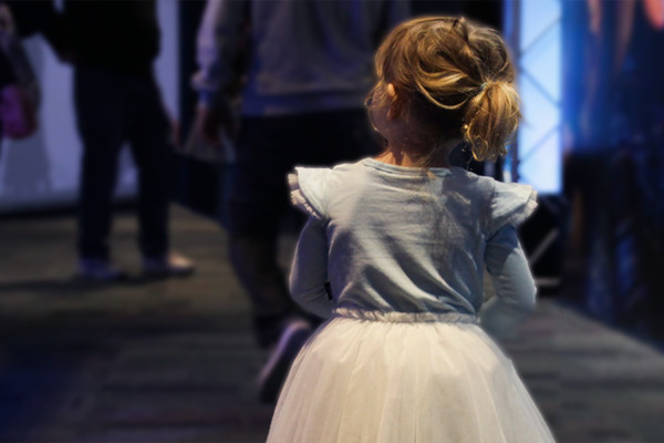 A young girl in a fairy outfit following a crowd of adults inside scitech