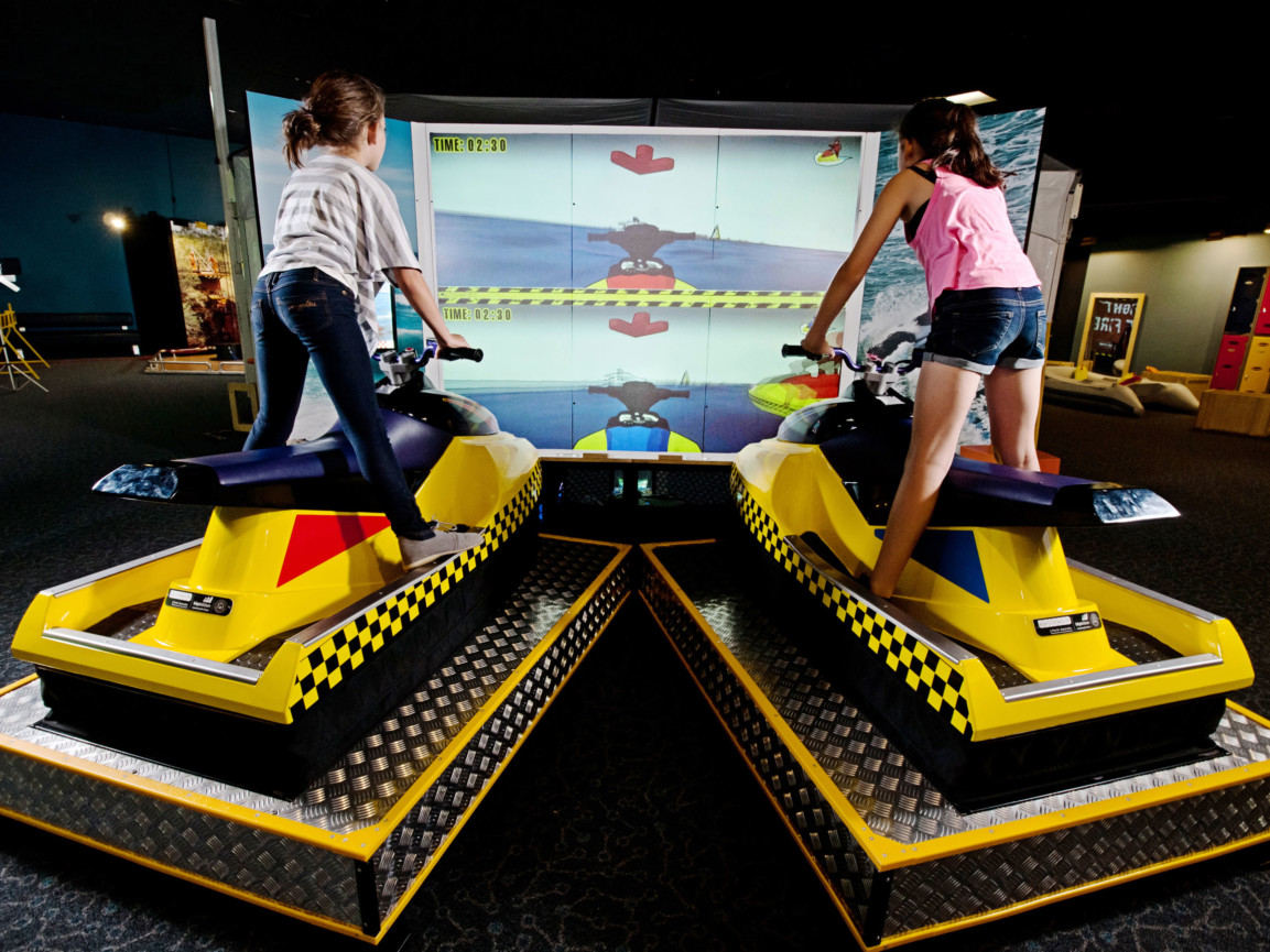 Two girls riding the jet ski simulator in the Rescue exhibit.