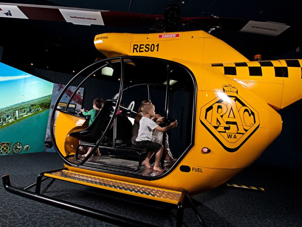 A group of children flying a helicopter simulation in the Rescue Exhibition at Scitech.