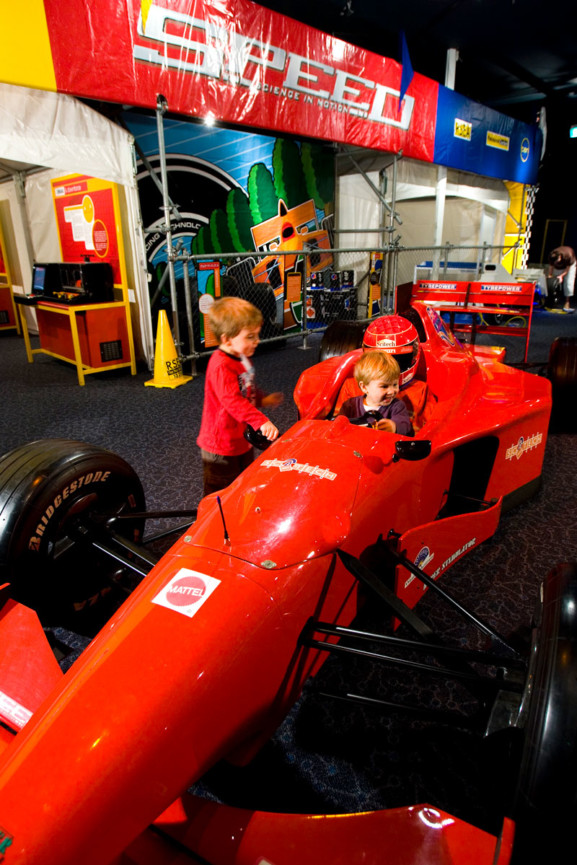 Two young boys playing in a formula one replica race car in Scitech's Speed exhibition.