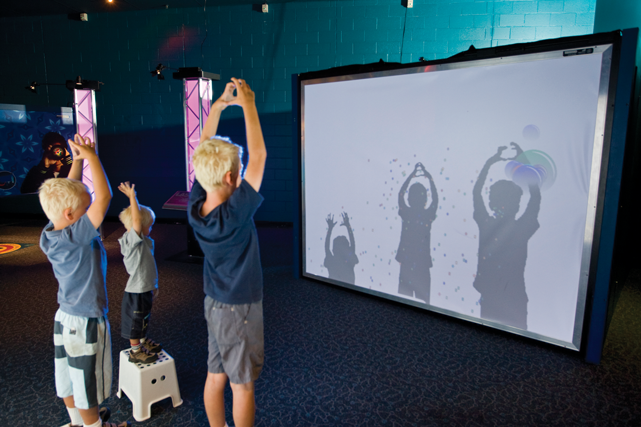 Three young boys making shadows on large white screen.