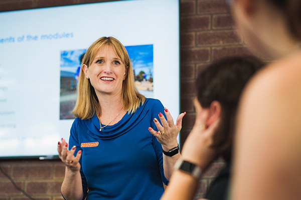 woman presenting to a group, her hands are up and she looks engaged