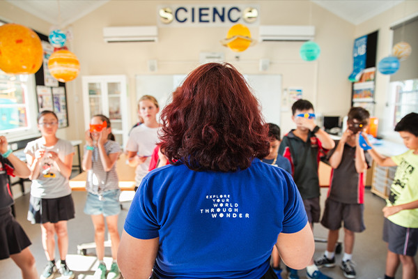 A science presenter facing a group of children wearing face masks.