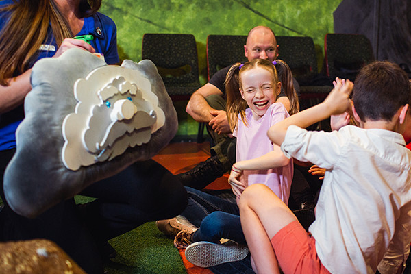 A young girl looking away from a pillow made into a cloud, shes laughing.
