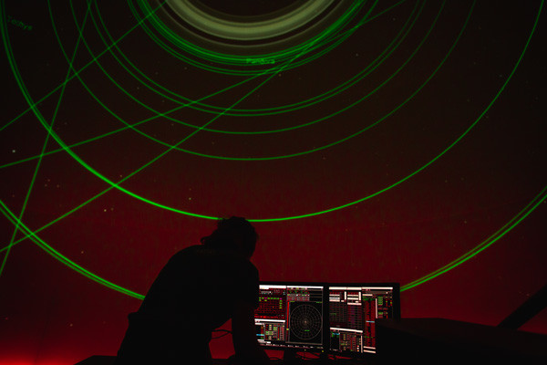 A planetarium presenter standing at the computer in front of the screen, showing a laser light show.