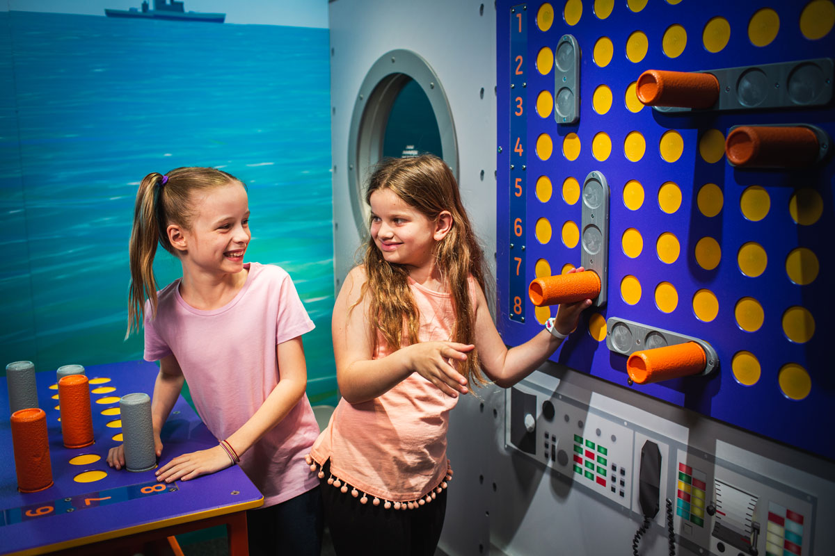 Two girls smiling at eachother while playing a life size game of battleships