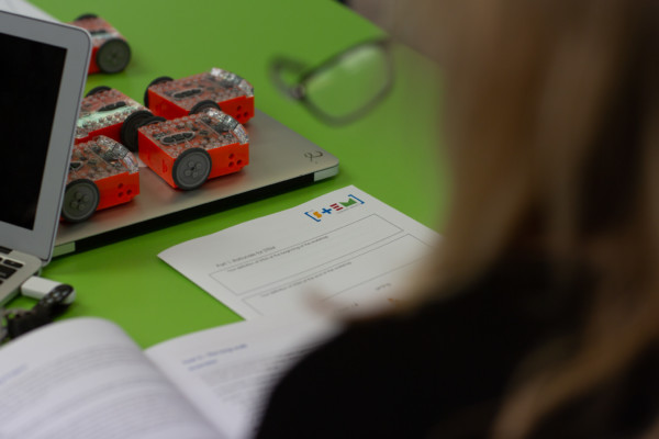 Overlooking womans shoulder with laptops, paper and robots on a table