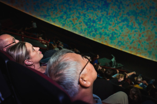 Three adults sitting in the planetarium theater, watching show.