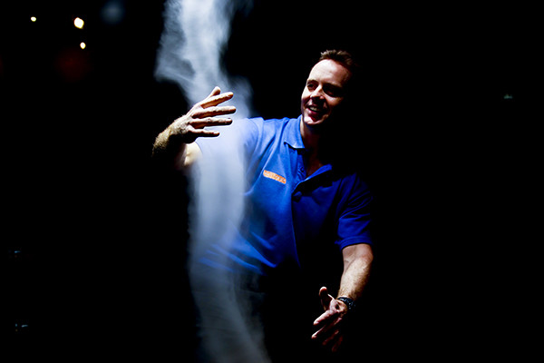 A man in a dark room holding his hands in a cloud of white smoke.