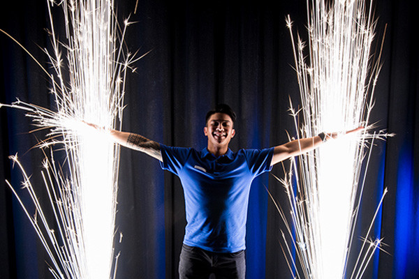 A man standing with his arms out and bright electricity light exploding behind him.