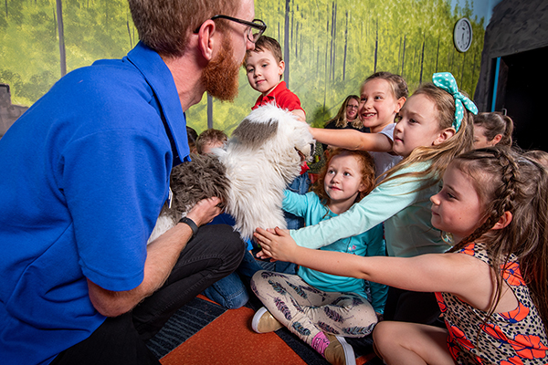 A man holding a dog hand puppet for a group of children to pat.