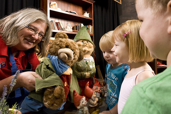 A woman holding a bear hand puppet to three young children