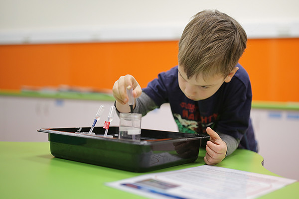 A small boy playing with a pipette and water in a science lab.