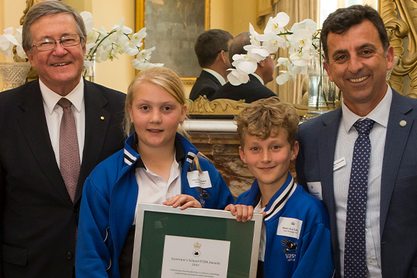 Two school children accepting a framed award with two professional middle aged men.