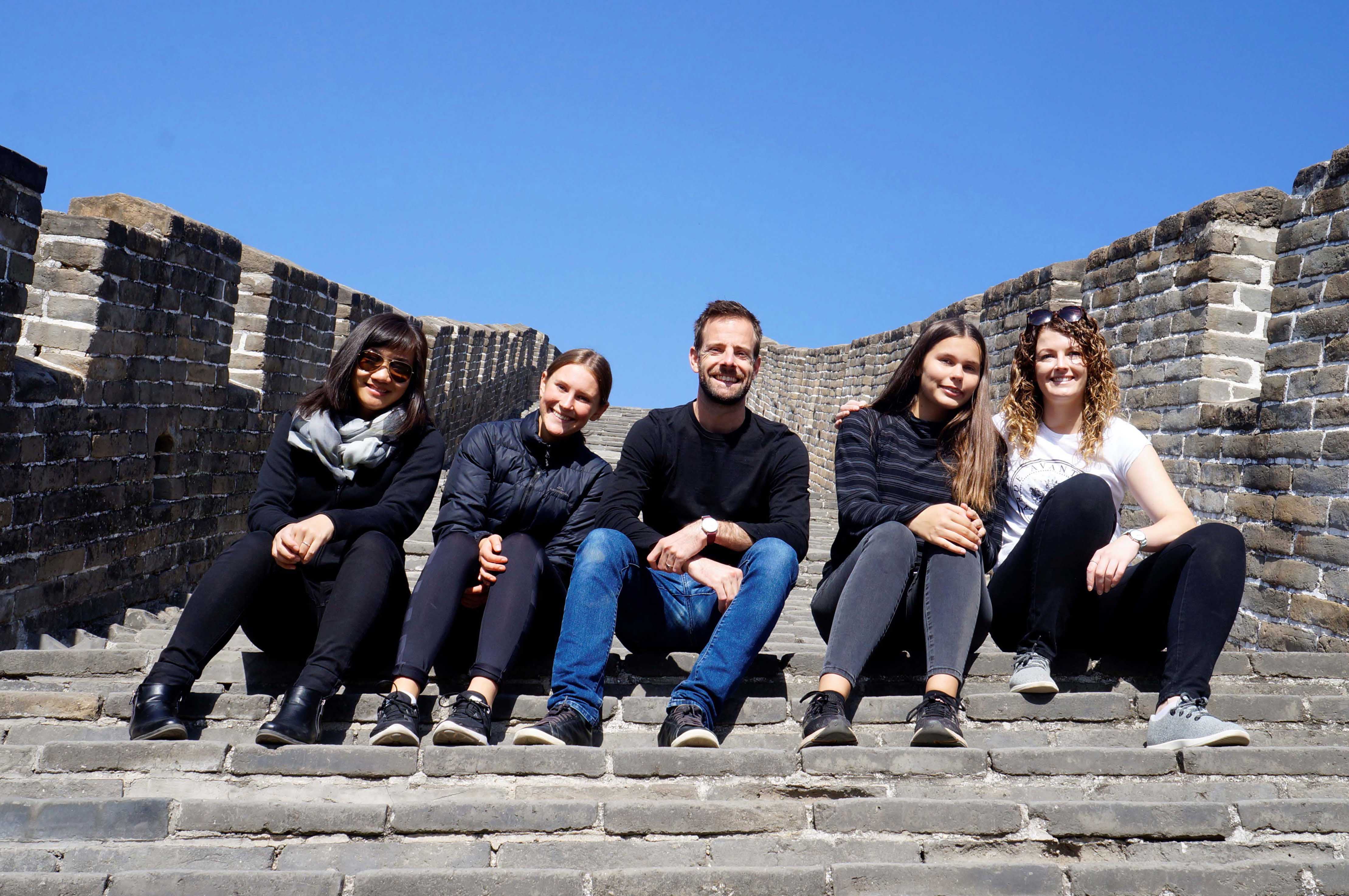 Five smiling adults sitting on a cement staircase on a sunny day in China from the Beijing Bound program