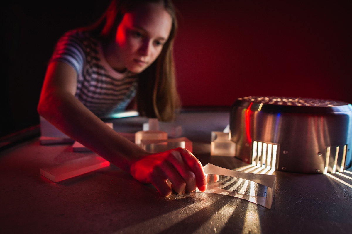 A young girl plays with optical components such as prisms and lenses.