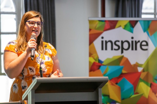 A smart casual woman giving a presentation at an event called Inspire