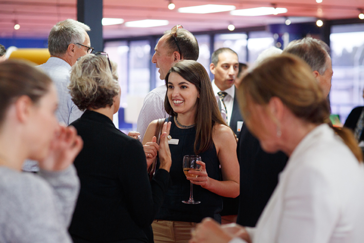 A group of people mingling at a corporate function, some holding glasses of wine.