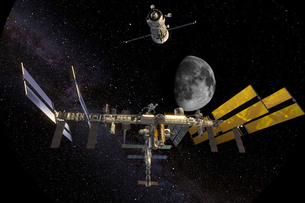 Photo of the International Space Station flying through the starry sky, with the moon in the background.