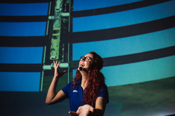 A science presenter talking to the audience at the front of the planetarium dome.