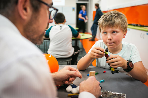 A young boy constructing a lego vehicle with help from an adult.