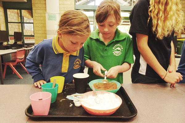 Two young children combine materials in a bowl.