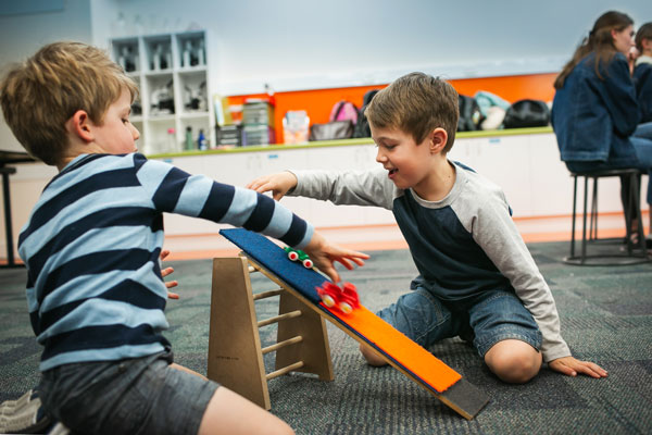 Two young boys racing toy cars down a ramp.