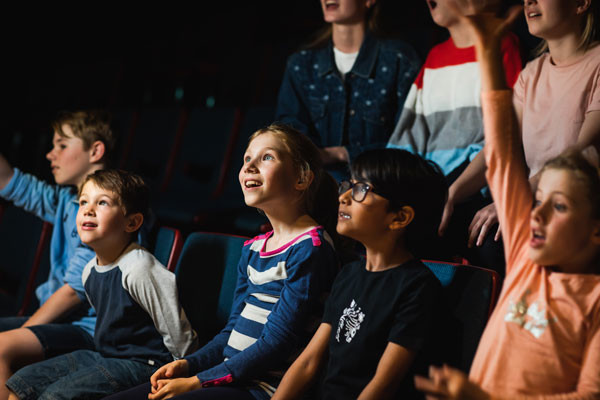 A group of young students watching a spacedome show, looking up and smiling.