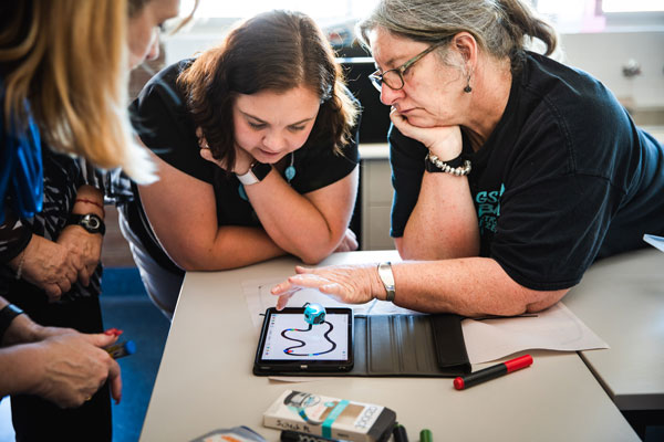 A group of teachers looking at an iPad and robot program on a desk.