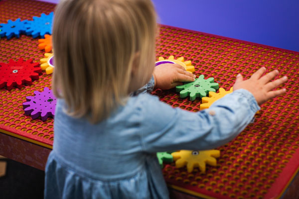 A young child plays with colourful cogs on a board.