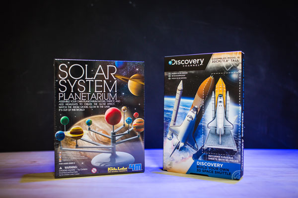 A solar system model toy and a rocket ship model toy, displayed in their boxes for The Discovery Shop.