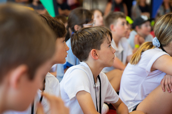 A group of school students sitting on the ground looking at a presentation.