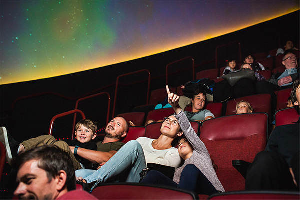 Adults and kids in the planetarium theatre, looking up at the screen.