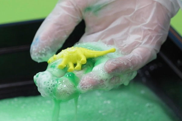Hands-on science experiment with toy dinosaur and bubbles.