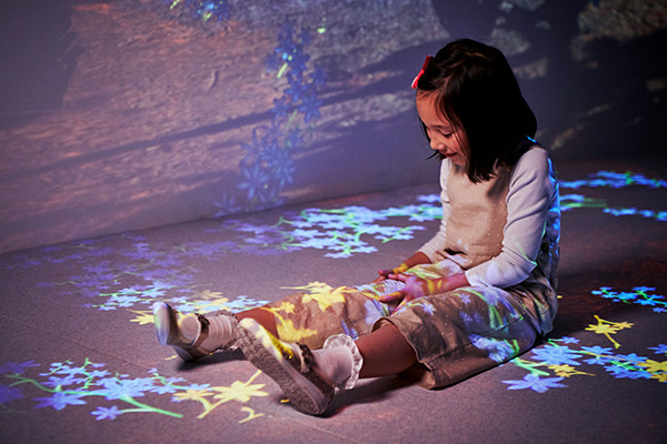 Girl sitting on floor looking at colourful projections over her legs