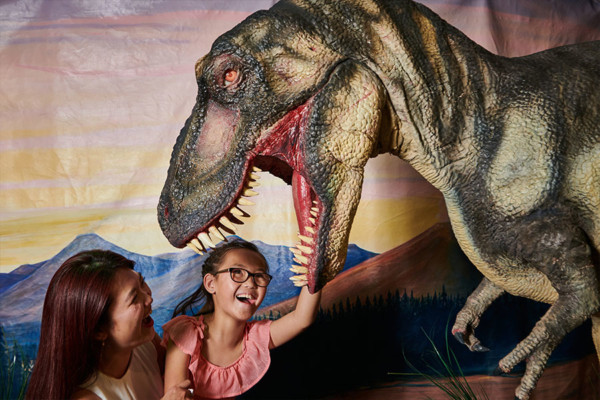 A young girl and her mother smiling up at an animatronic Tyrannosaurus rex.