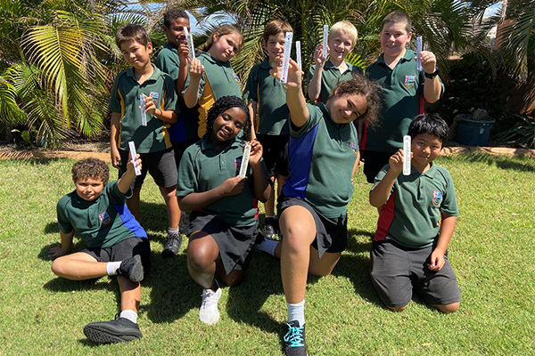 Students kneeling together holding temperature gauges and smiling.