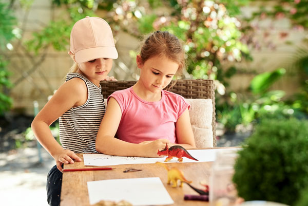 Sisters making craft dinosaurs on outdoor table