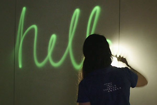 A woman writing hello using phosphorescence on a wall.