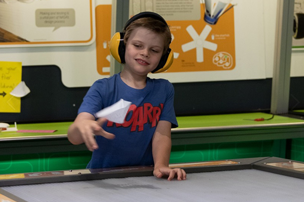 A young boy wearing ear muffs playing with a paper.