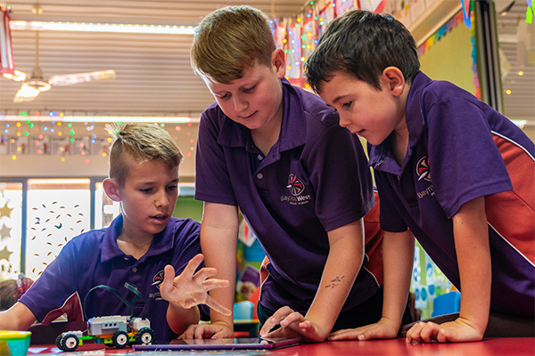 Three young boys standing over robotic toys.