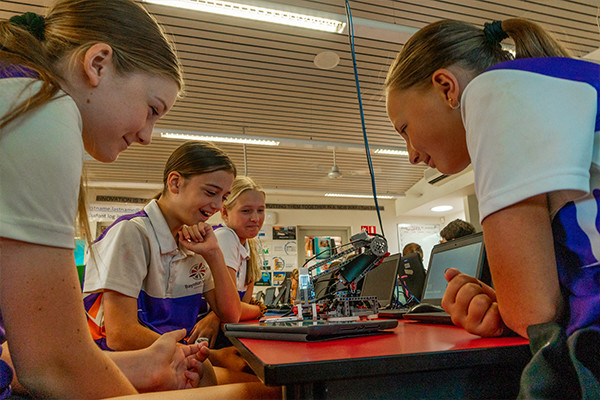 Three girls smiling while looking at a robotic toy.