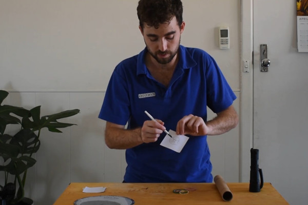 A man in a blue shirt drawing a constellation on a small square piece of paper.