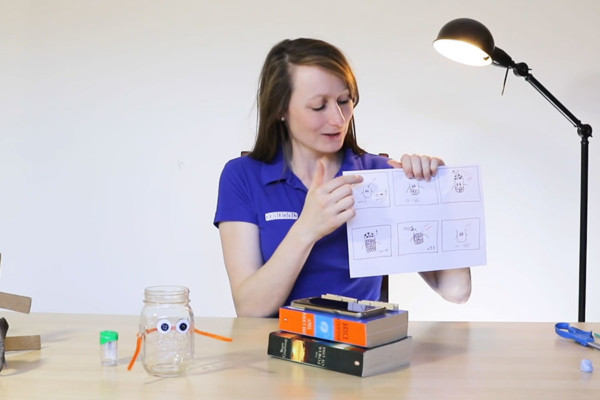 A woman holding up a piece of paper with a jar and book on a desk.