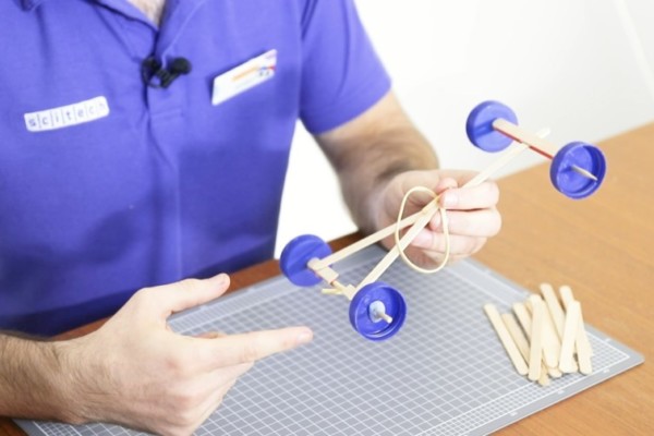 Scitech presenter holding car model made of Popsicle sticks and milk bottle caps.